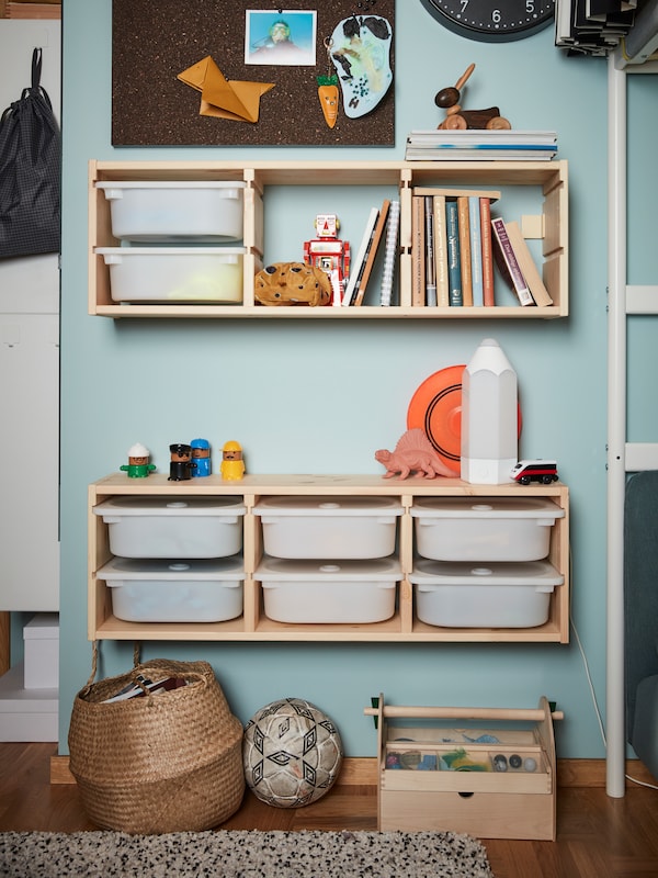 A wall with two units of TROFAST wall storage which hold TROFAST storage boxes, toys, books and a PELARBOJ LED table lamp.