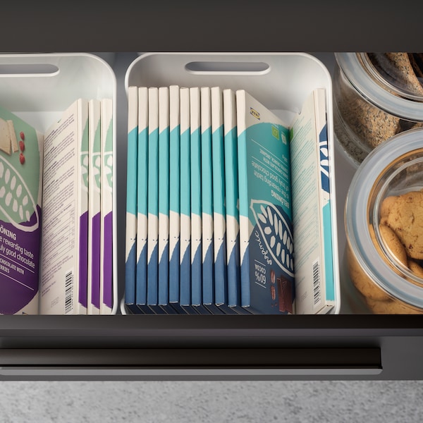 A pulled-out kitchen drawer revealing BELÖNING chocolate tablets neatly stacked inside VARIERA boxes and two glass jars.