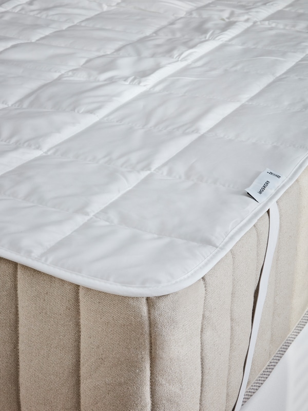 A corner of a mattress on which an ÄNGSKORN mattress protector has been fastened in place.