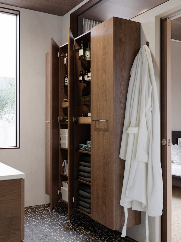 High cabinets with wooden doors attached to the wall showing towels, toiletries and boxes arranged in a neat way.