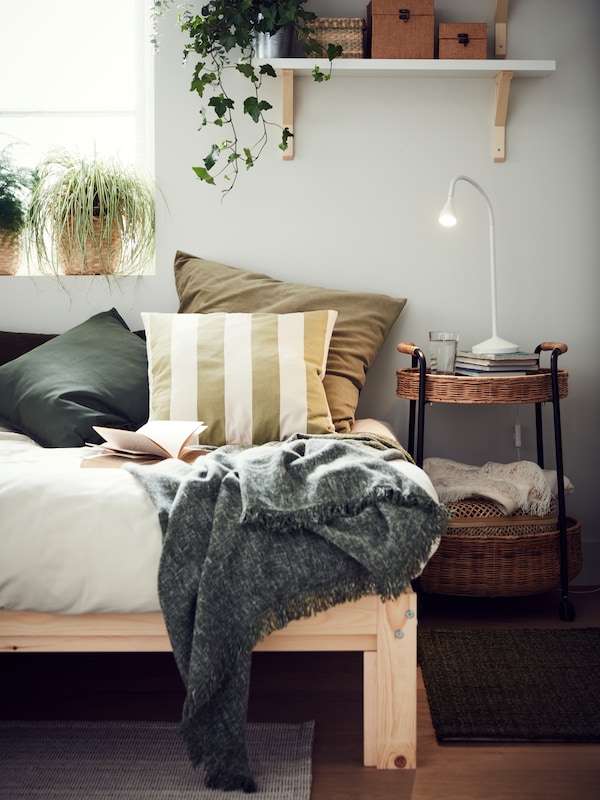 Cushions in different cushion covers and a dark green INGRUN throw are on a pine NEIDEN bed near a window.