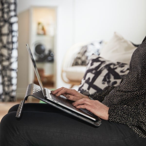 A person sitting on a Vansbro bright green 2-seat sofa-bed with a black BRÄDA laptop support and a laptop.