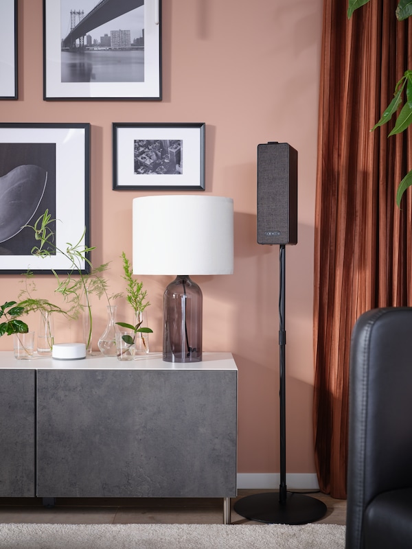 A tv stand with doors in a charcoal gray color, picture frames above mounted against a pink wall.