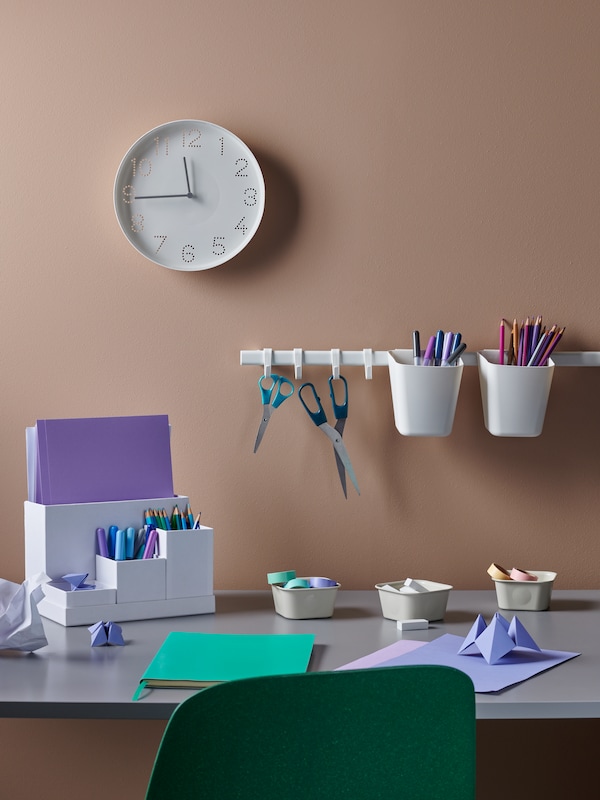 A workspace made up of a desk, a TROMMA clock, scissors on a SUNNERSTA rail, and colorful accessories in a TJENA organizer.