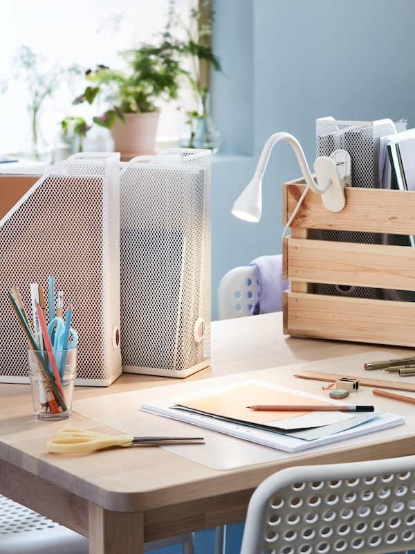 A kitchen table serving as a workspace, with a SKVALLRA desk pad, DRÖNJÖNS magazine files and other office accessories.