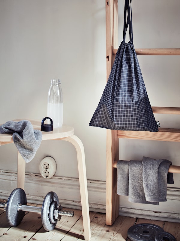 An area along the side of a room scattered with weights, an IKEA 365+ water bottle, KORNAN washcloths, and a RENSARE gym bag.