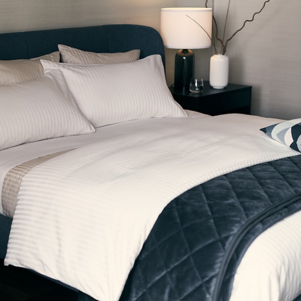 A blue TUFJORD upholstered bed with NATTJASMIN bed linen and a MJUKPLISTER bedspread stands in a corner.