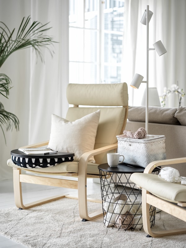 A beige POÄNG armchair with a black KVISTBRO storage table and a reading lamp next to it.