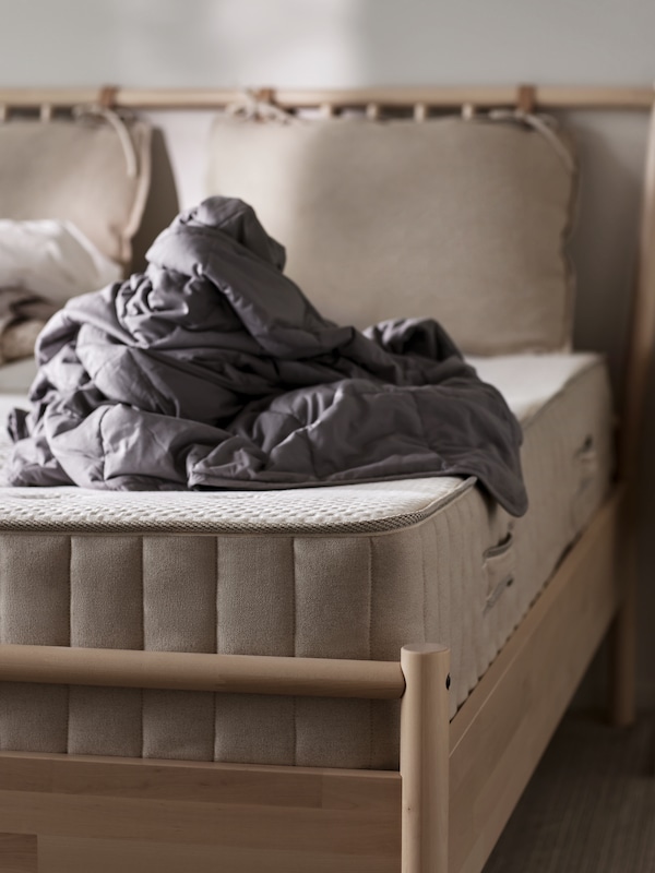 A VATNESTRÖM pocket sprung mattress with a crumpled up ODONVIDE weighted blanket on top of it lies on a bed frame.