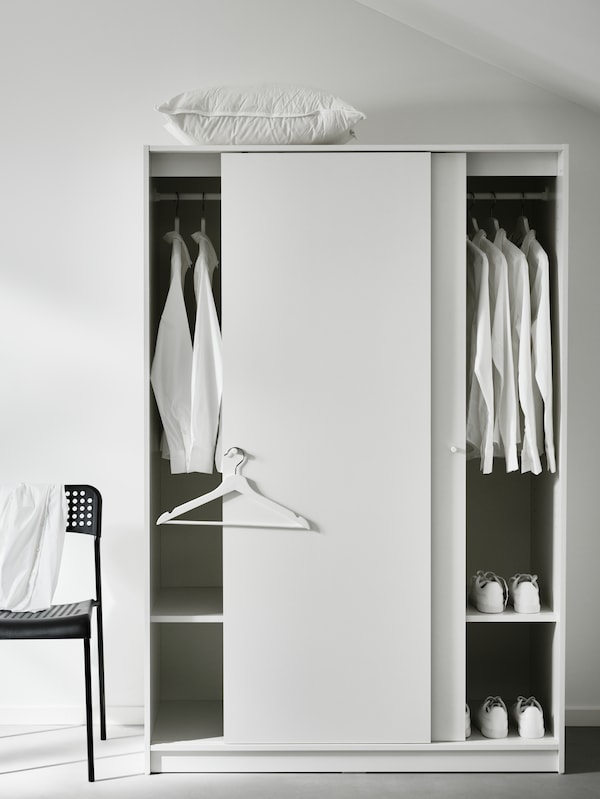 A white KLEPPSTAD wardrobe with both the doors open, showing white shirts on the hanging rails. A black chair is beside it.