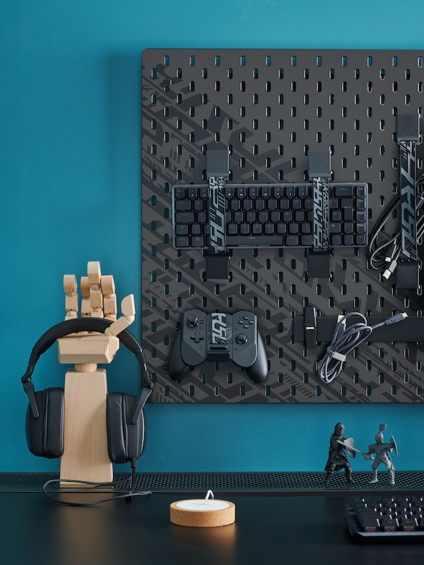 A desk with gaming accessories on a black UPPSPEL pegboard combination, and a headset on a LÅNESPELARE accessories stand.