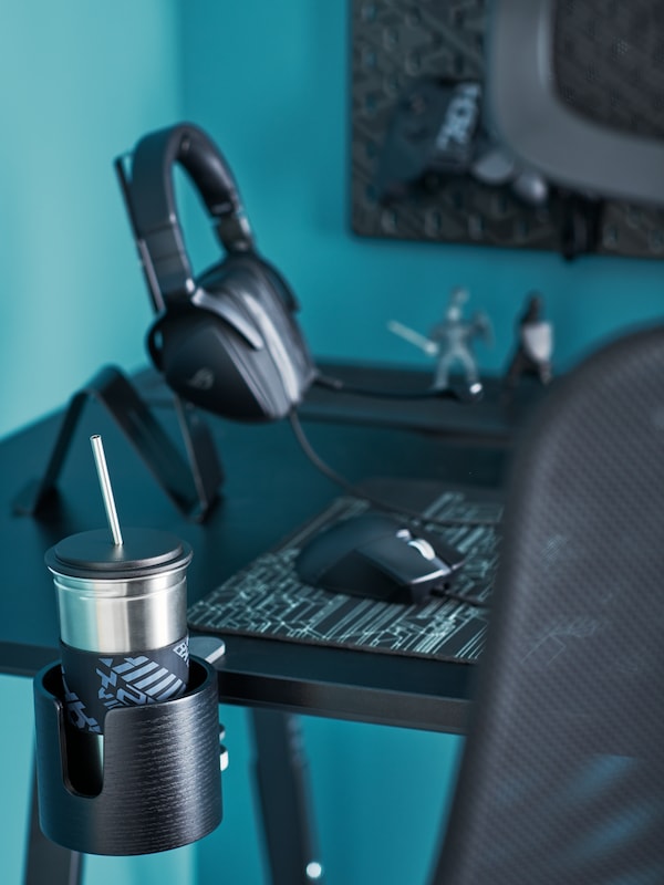 A gamer's desk with a LÅNESPELARE mug and mug holder, a LÅNESPELARE gaming mouse pad and a headset on a MÖJLIGHET stand.