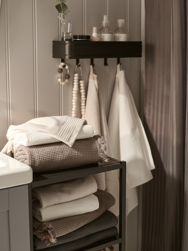 An anthracite ENHET base frame with towels on its shelves near a LILLASJÖN wall shelf holding towels and other items.