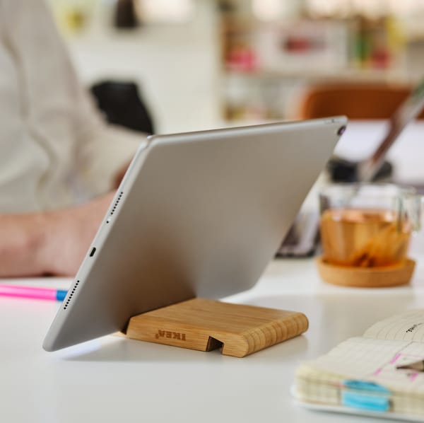 A bamboo BERGENES holder for mobile phone/tablet sits on a desk holding a tablet near a diary, a pen and a mug.