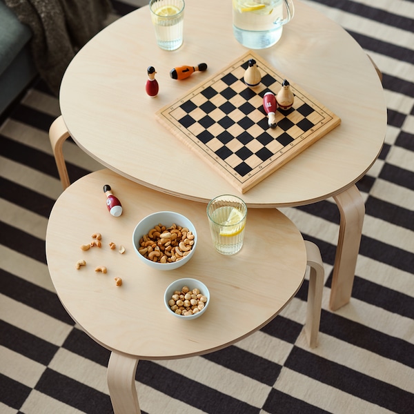 A board game, two bowls of snacks and lemonade on top of SVALSTA nest of tables in birch veneer.