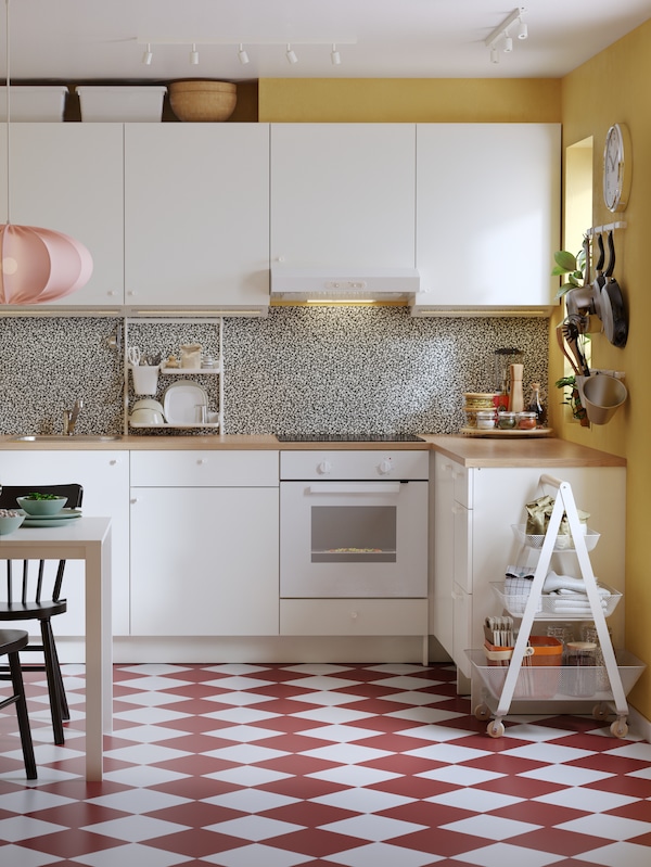 An eclectic kitchen with red and white checkered floors, yellow walls and KNOXHULT base and wall cabinets in white.