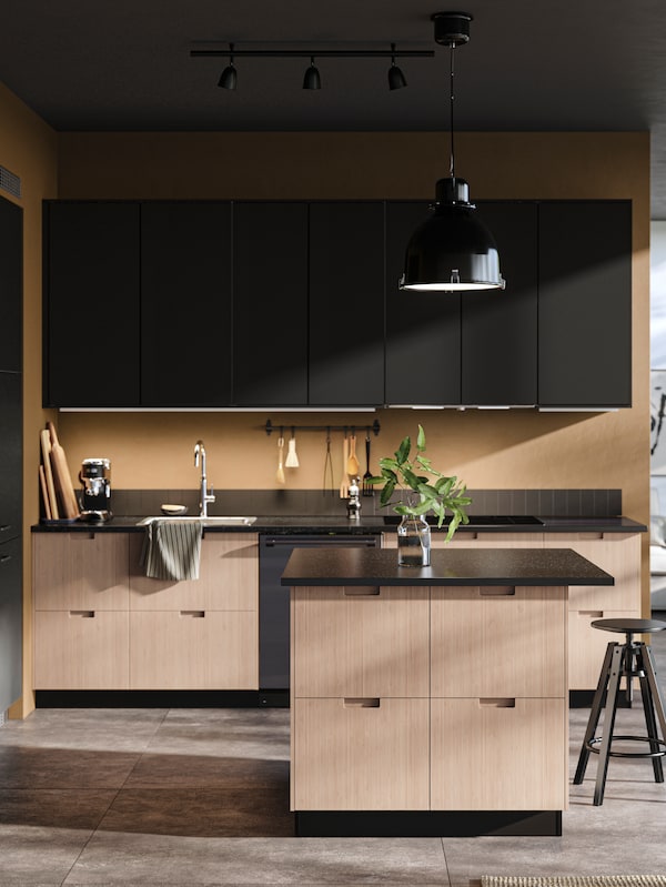 A kitchen with stone floors and kitchen island, FRÖJERED fronts in light bamboo and KUNGSBACKA fronts in anthracite.