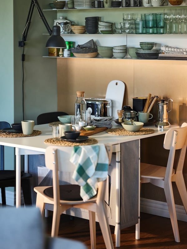 A cozy dining nook with ash LISABO chairs and a KALLHÄLL gateleg table with storage set up for a meal for four people.