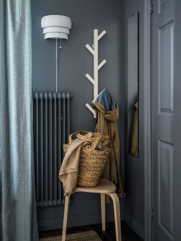 The branch-like shape of a wall-mounted, white TJUSIG hanger contrasts against a hallway painted grey.