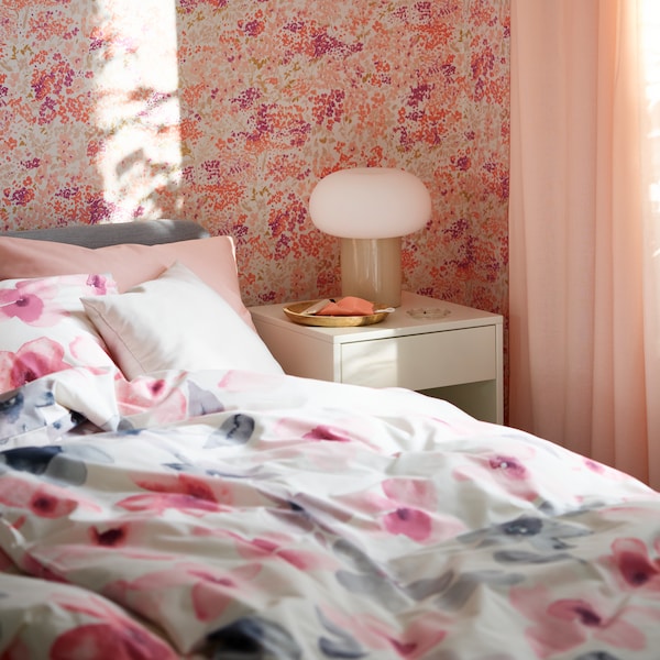 A SLATTUM upholstered bed with LAPPNYCKLAR bed linen stands beside a VIKHAMMER bedside table with a DEJSA table lamp.