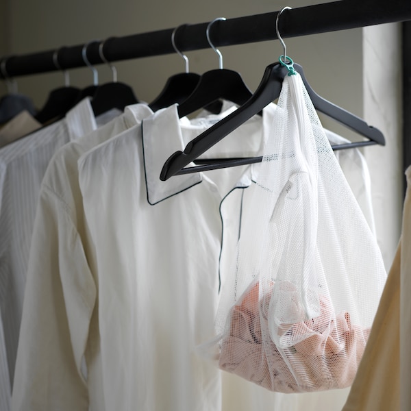 Various clothes on black BUMERANG hangers placed on a black rod. A white SLIBB washing bag is attached to one of the hangers.