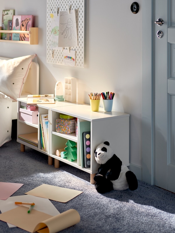 A toy panda leans against one of two white SMUSSLA bedside tables/shelf units standing beside each other near a child’s bed.