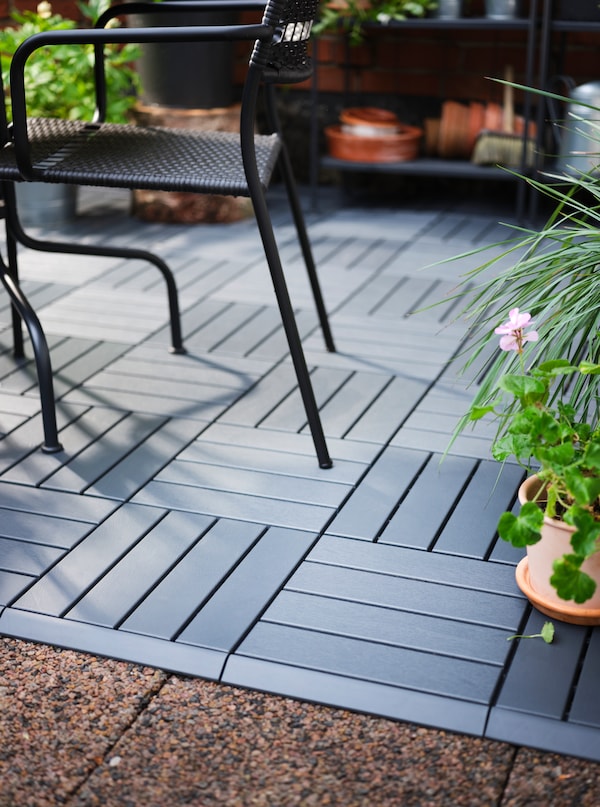 A LÄCKÖ chair with armrests sits on a terrace which is partly covered in dark grey RUNNEN floor decking.