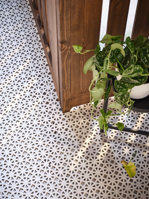 A plant in a pot on an OLIVBLAD plant stand on a balcony covered in light grey ALTAPPEN floor decking.