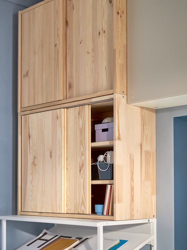 Two IVAR wooden cabinets with sliding doors with one open, revealing boxes, books and personal items.