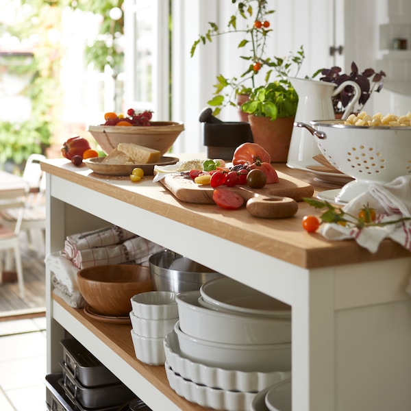 A TORNVIKEN kitchen island has dishes stacked underneath and fruits, cheese and food resting on top.