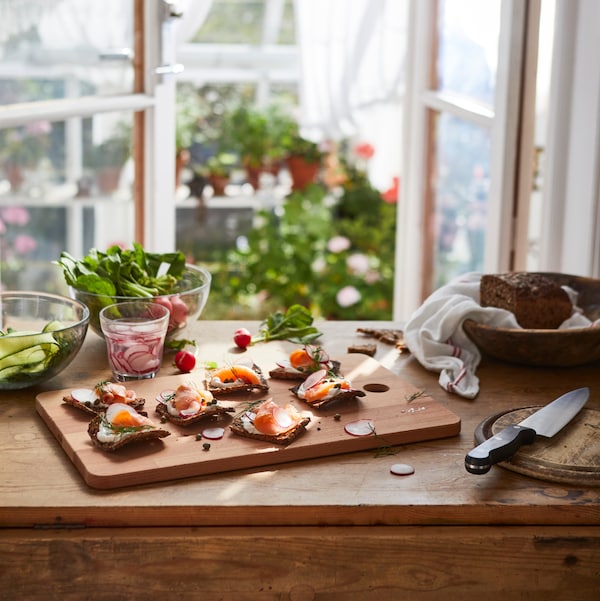 A wooden chopping board has food on it, being prepared to be served, with a VARDAGEN cook’s knife next to it.