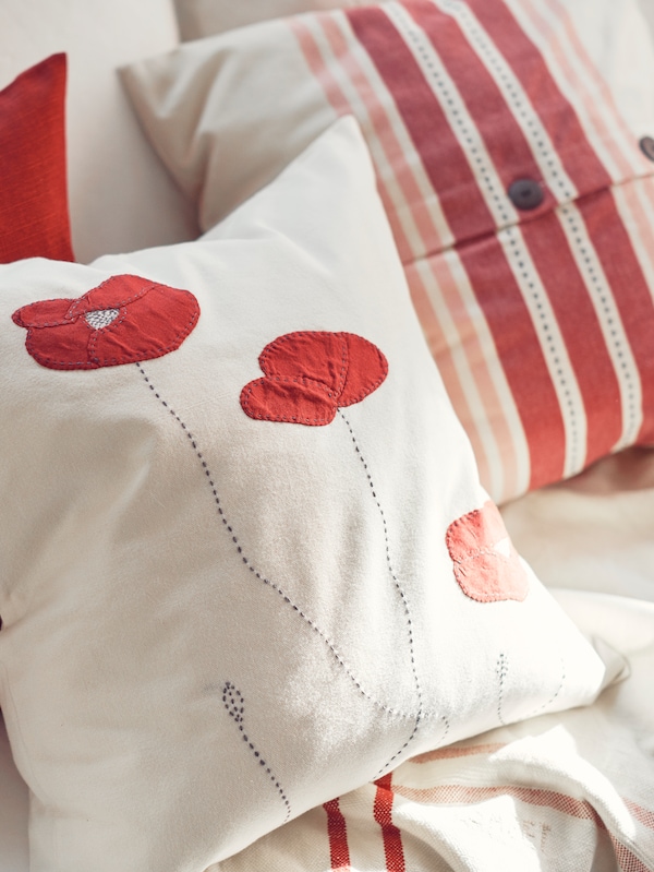 A cushion with a SILOMAL cover with a floral pattern lies next to a cushion with a VEDMAL cover with a striped pattern.