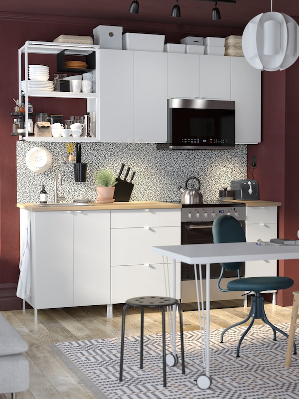 An ENHET kitchen in white, with a white LAGKAPTEN/KRILLE desk, a blue BJÖRKBERGET swivel chair and a black MARIUS stool.