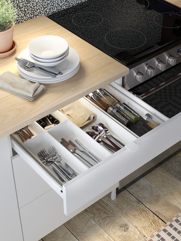 A white ENHET kitchen drawer unit with the top drawer open showing an UPPDATERA cutlery tray holding cutlery and utensils.