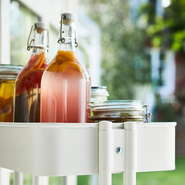 A RÅSKOG kitchen cart on wheels has two bottles of colored juice on the top shelf.