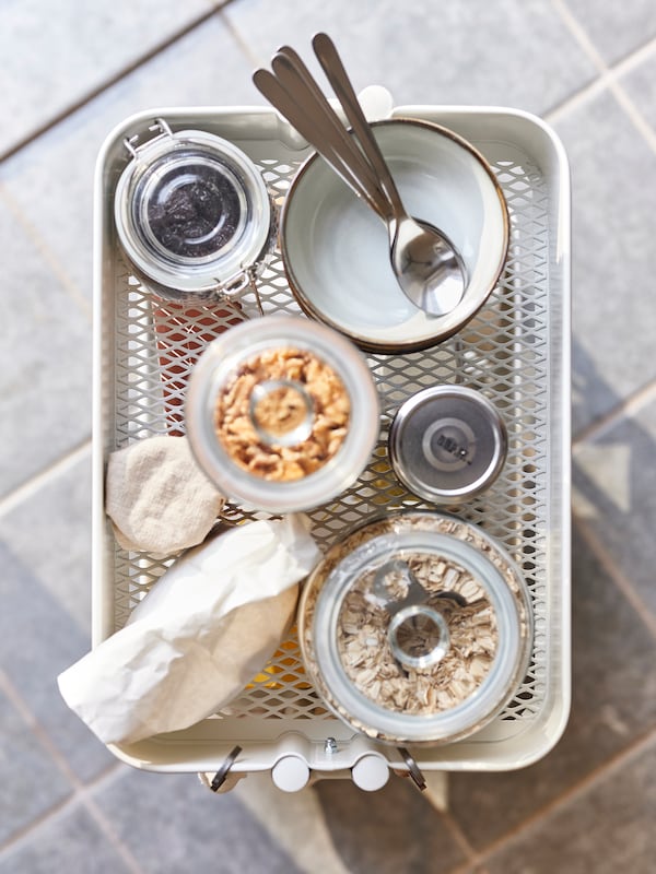 Stacked GLADELIG bowls and VARDAGEN glass jars filled with dry goods in the top compartment of a white RÅSKOG cart.