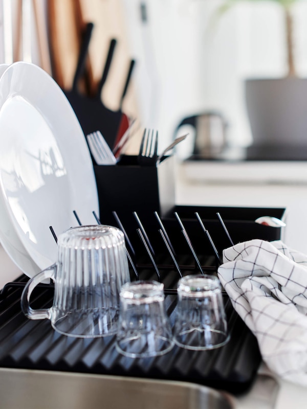 Plates and glassware next to the sink on a kitchen drying rack. 