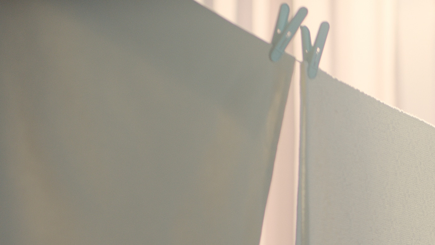 Textiles, three white and one pink, on a clothesline, the arms and torso of a person in a brown jumper in the background.