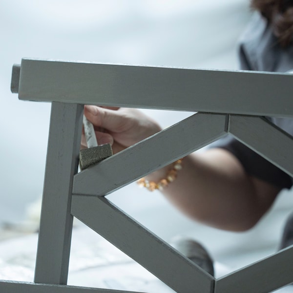 The hand of a person doing maintenance work on a grey BONDHOLMEN chair with armrests.