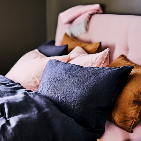 The head of a pale pink IDANÄS upholstered storage bed, covered with bedding including DYTÅG bed linen.