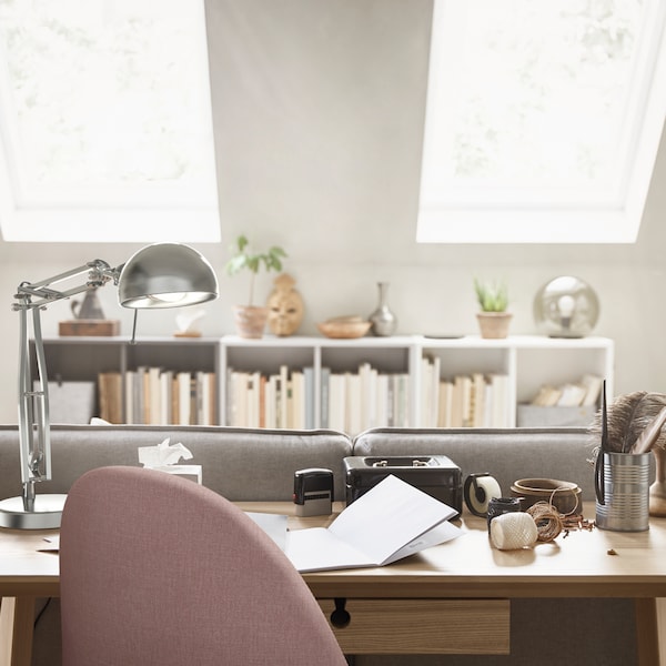 The top of a pink work chair that’s in front of a LISABO desk with a work lamp on it and a row of white shelves at the back.