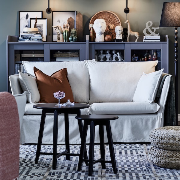 Two nest of tables in front of a light 2-seat sofa on a patterned rug. Two HAUGA glass door cabinets are behind it.