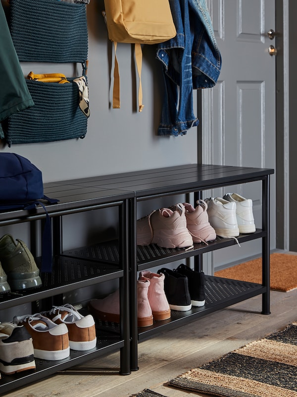 Two PINNIG benches with shoe storage holding shoes and boots stand in a hallway. NORDRANA hanging storage hangs above.