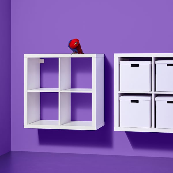 Two white KALLAX shelving units, one containing white boxes, are mounted side by side on a purple wall.