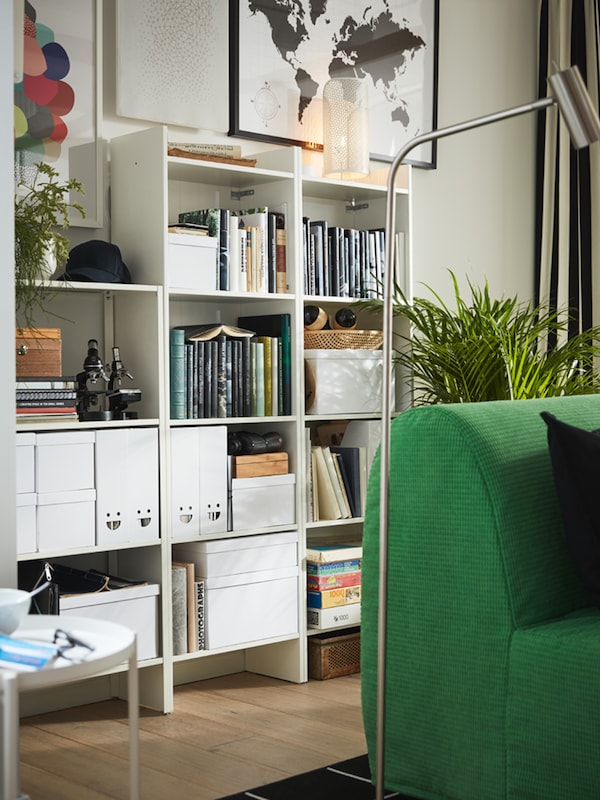 White bookcases, books, white storage boxes with lids, white magazine files, potted plants, art on the wall.