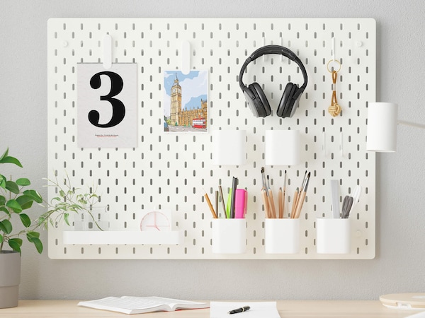 White storage pegboard with hooks & cups holding pencils, markers and headphones.