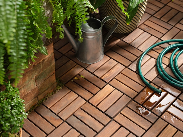 Wooden patio flooring with wooden planters holding ferns, a gardening pitcher & hose. 